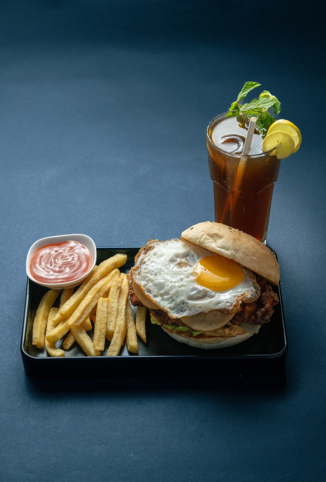 Fried chicken burger with a fried egg, fries and iced tea